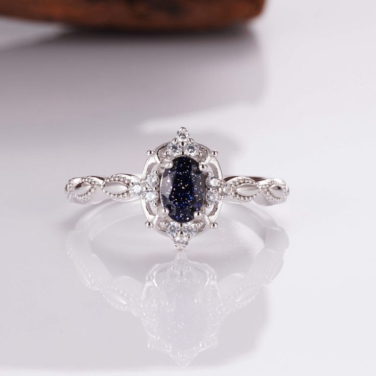 an oval shaped ring with a blue stone surrounded by white diamonds on a reflective surface