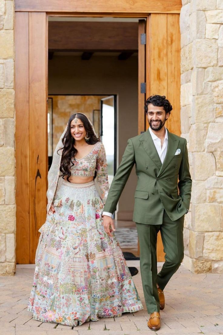 a man and woman walking out of a building together in front of a door wearing green suits