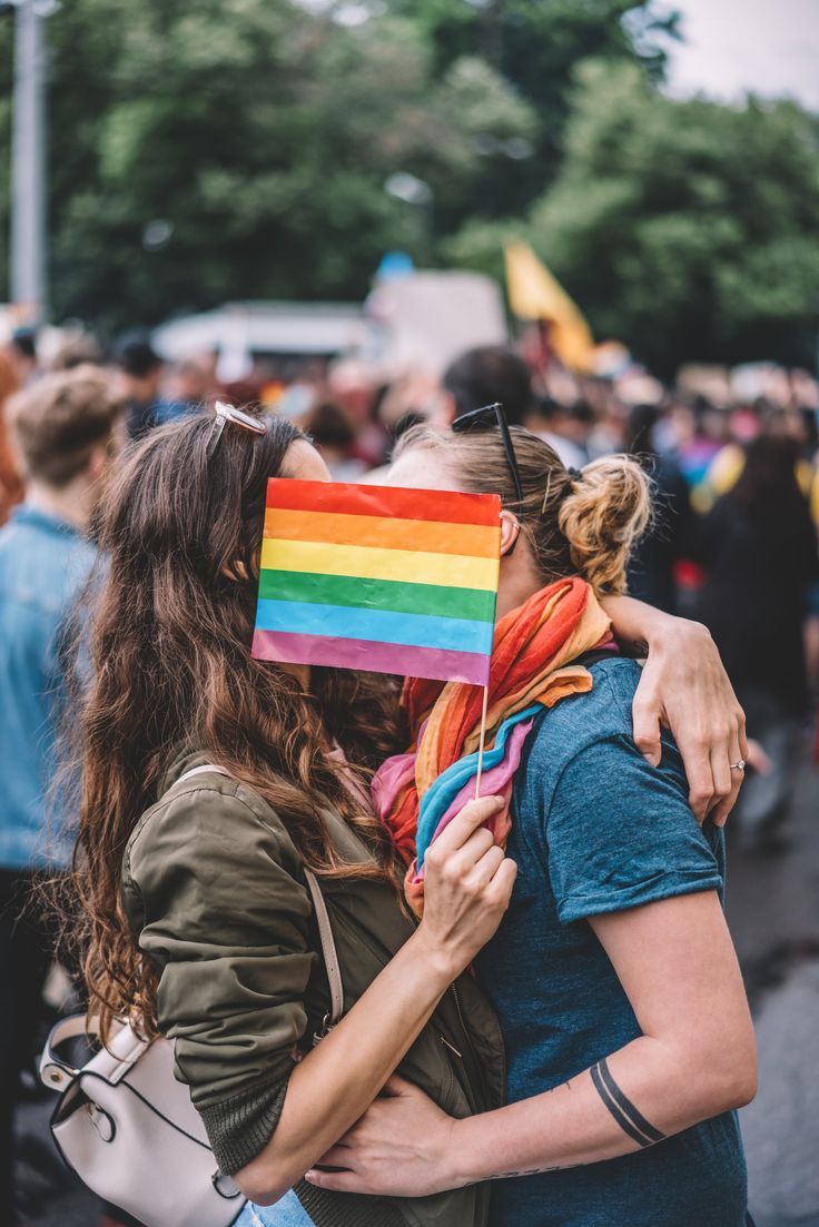 two women hugging each other with a rainbow flag on their head