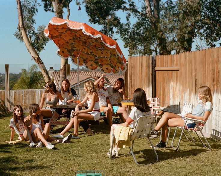 a group of young women sitting on top of a grass covered field next to a wooden fence