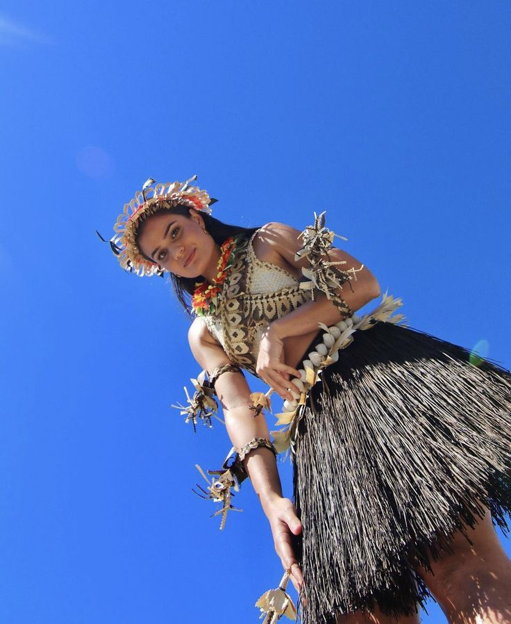 a woman in a hula skirt and headdress poses for the camera on a sunny day