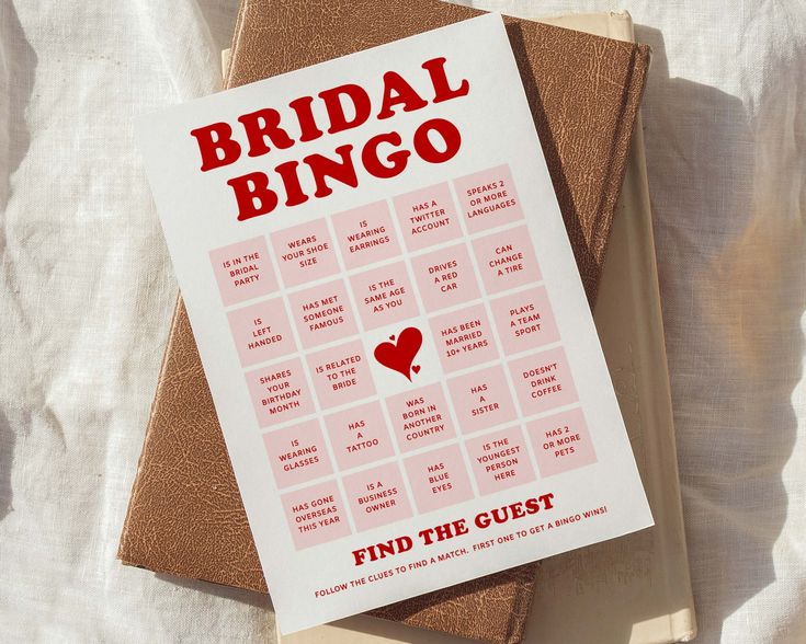 a bridal bingo game sitting on top of a bed next to a book titled find the guest