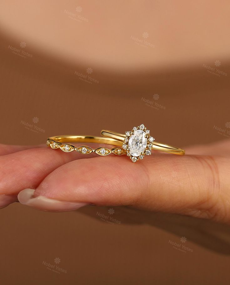 a woman's hand holding two gold wedding rings with diamonds on each band and an oval shaped diamond in the middle