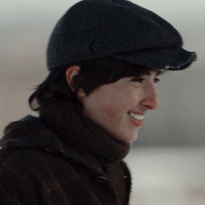 a young man wearing a black hat and scarf smiles at something while standing in the snow