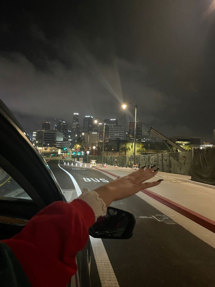 a person's hand reaching out the window of a car on a city street at night