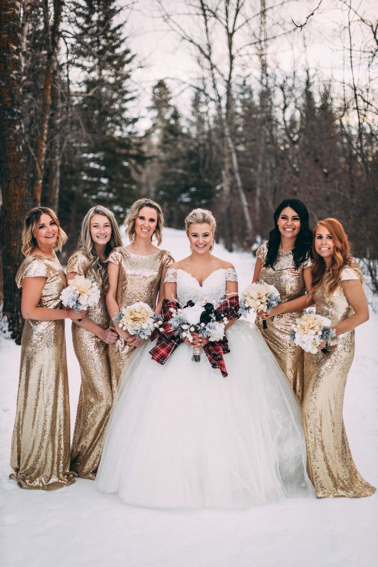 a group of women standing next to each other in the snow wearing dresses and holding bouquets