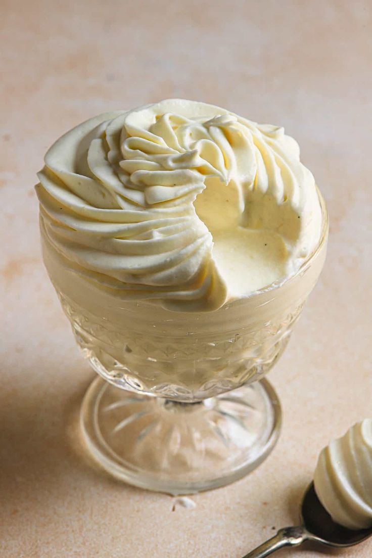 a dessert in a glass bowl with whipped cream on top and a spoon next to it