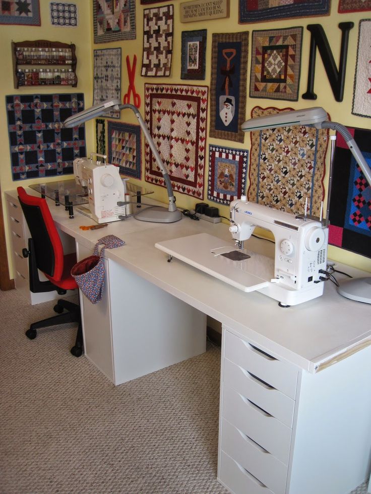 a sewing machine sitting on top of a white desk next to a red chair in front of a wall covered with quilts