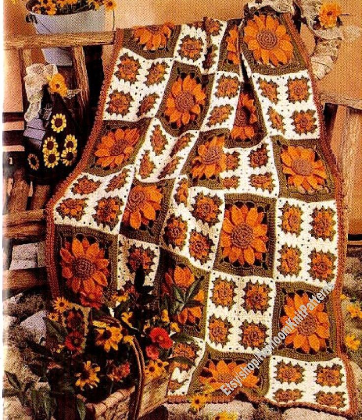 an orange and white crocheted blanket sitting on top of a wooden bench next to flowers