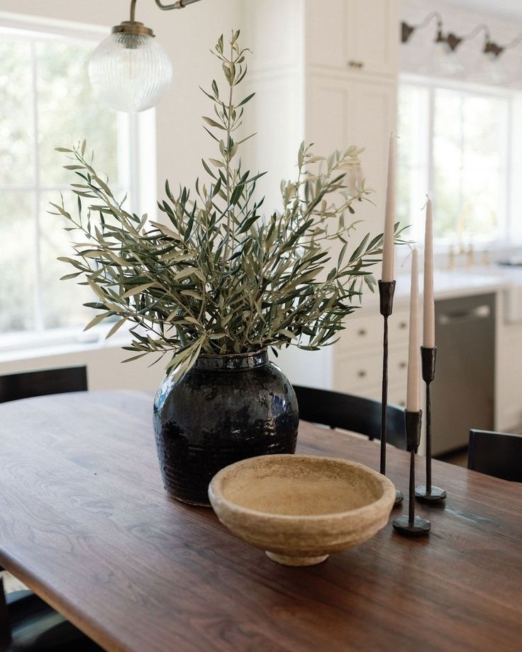 a wooden table topped with a black vase filled with greenery