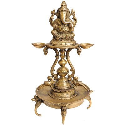 an ornate brass plate with ganesha on it's stand and two candles in the middle