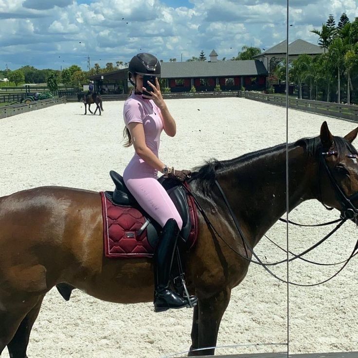 a woman in pink riding on the back of a brown horse while talking on a cell phone