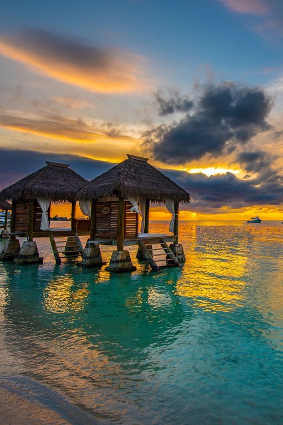 the sun is setting over the water and some huts are set up on stilts