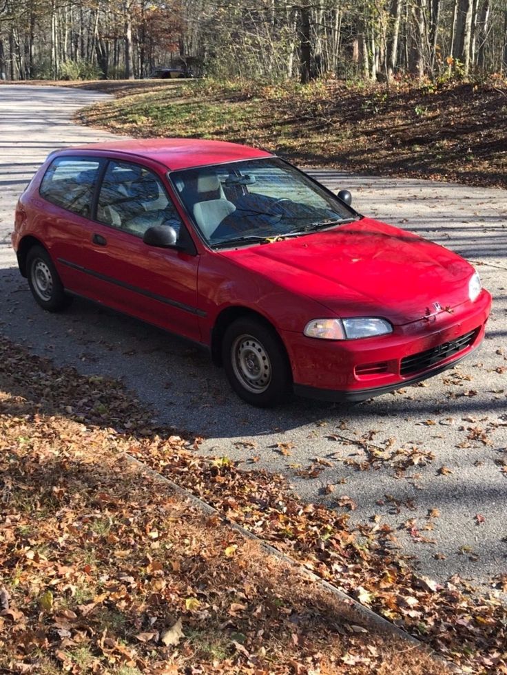 a red car is parked on the side of the road in front of some trees