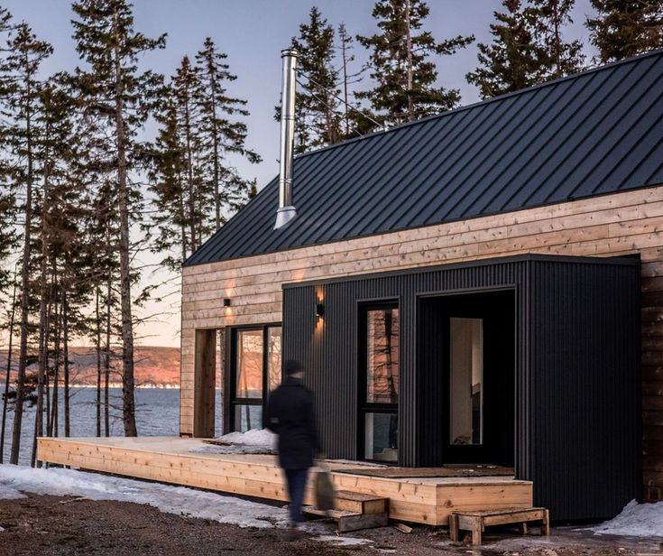 a small cabin sits on the shore of a lake at sunset with snow and pine trees surrounding it