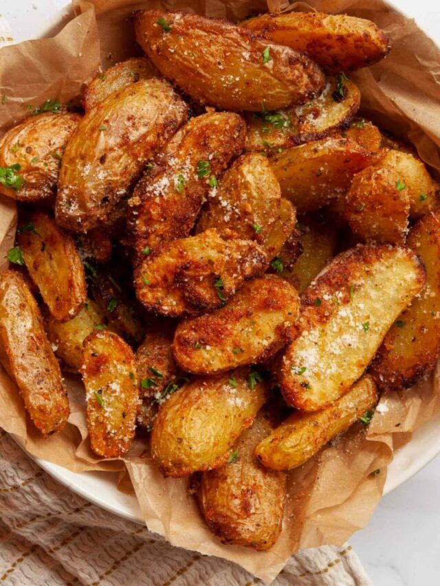 fried potatoes with parmesan cheese and herbs in a paper bowl on a table