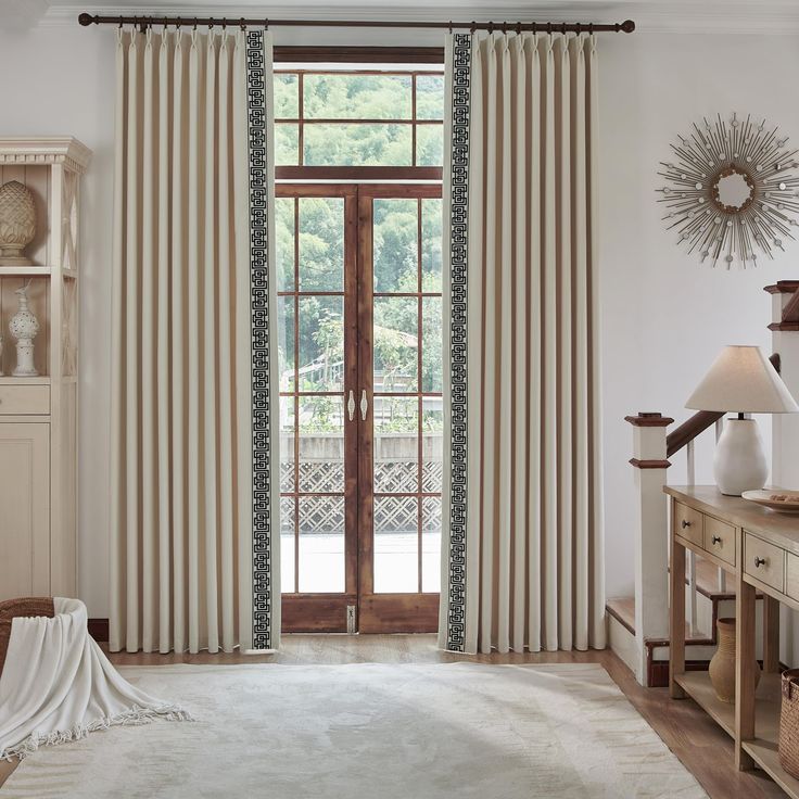 a living room filled with furniture and a large window covered in white drapes next to a wooden dresser