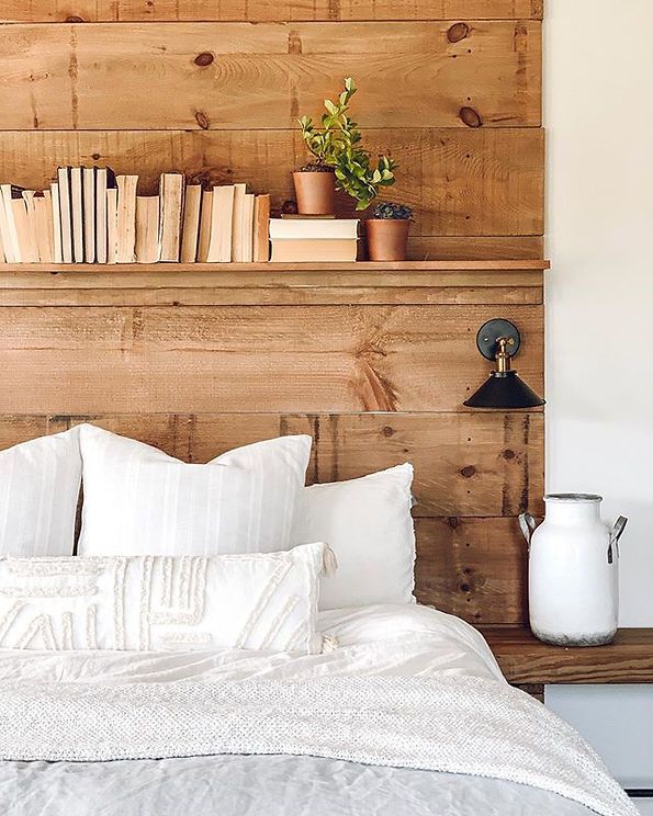 there is a bed with white pillows and books on the headboard, next to a wooden shelf