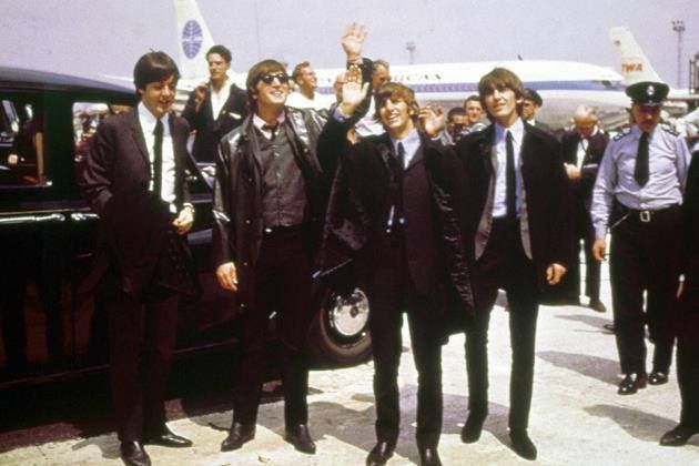 several people in suits and ties standing next to an old black car with a plane behind them