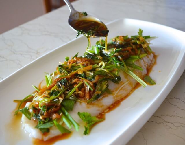 a white plate topped with fish covered in greens and sauce next to a spoon on top of it