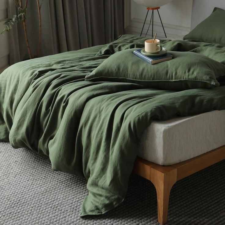 a bed with green sheets and pillows in a room next to a lamp on a table