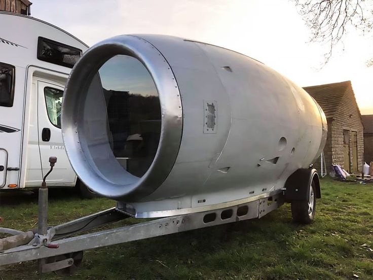 a large metal tank sitting on the back of a trailer in a grassy field next to a house