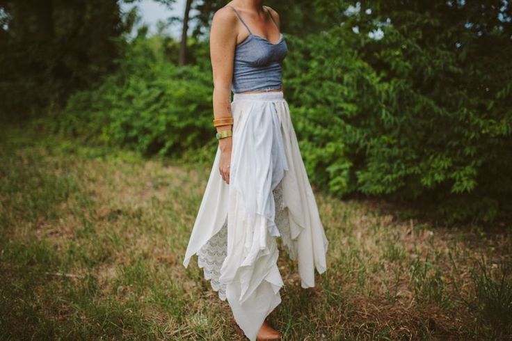 a woman standing in the grass wearing a white skirt and tank top with her hands on her hips