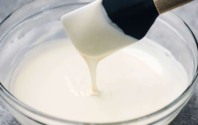 a glass bowl filled with white liquid and a wooden spoon sticking out of the top