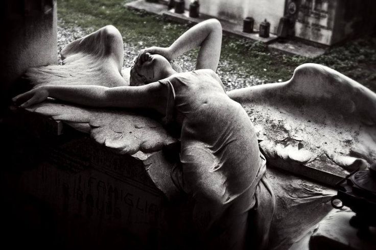 a woman laying on top of a wooden bench next to a cemetery filled with tombstones