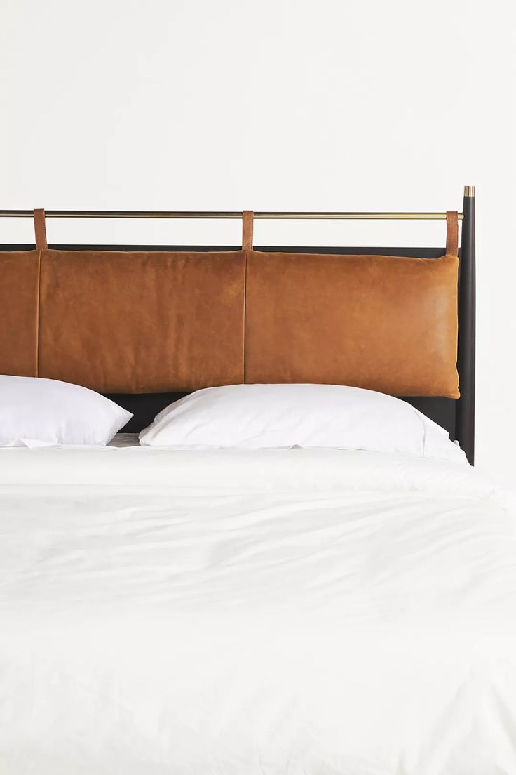 a brown leather headboard with two white pillows on top of the bed in front of a white wall