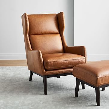 a brown leather chair and footstool in front of a white wall with an ottoman