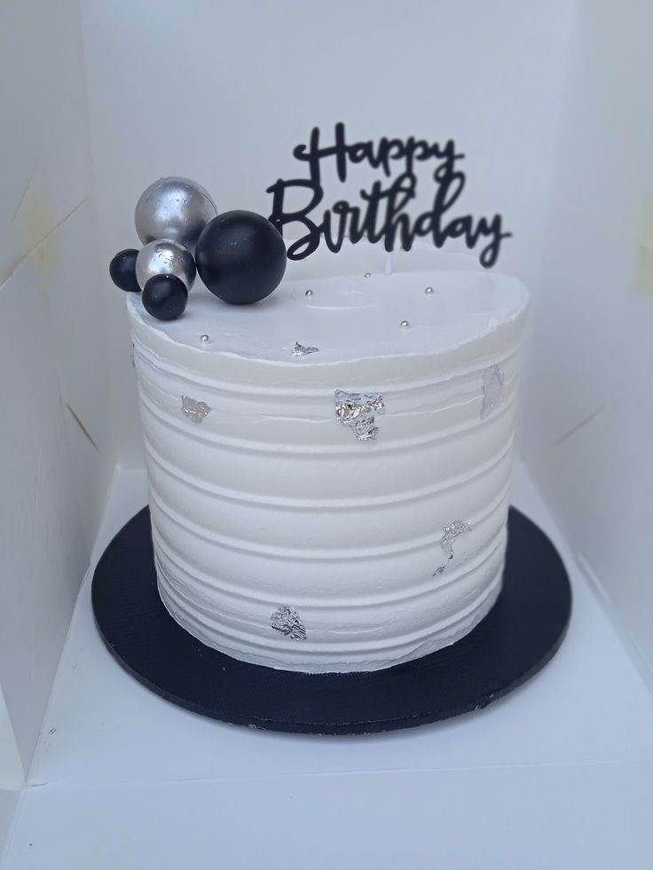 a white birthday cake with black and silver decorations