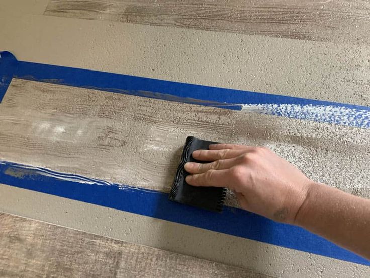 a person using a brush to paint a wall with blue tape on the bottom half of it