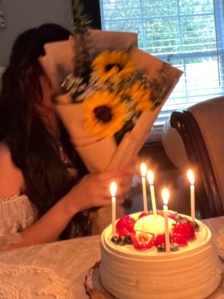 a woman sitting at a table with a cake and flowers