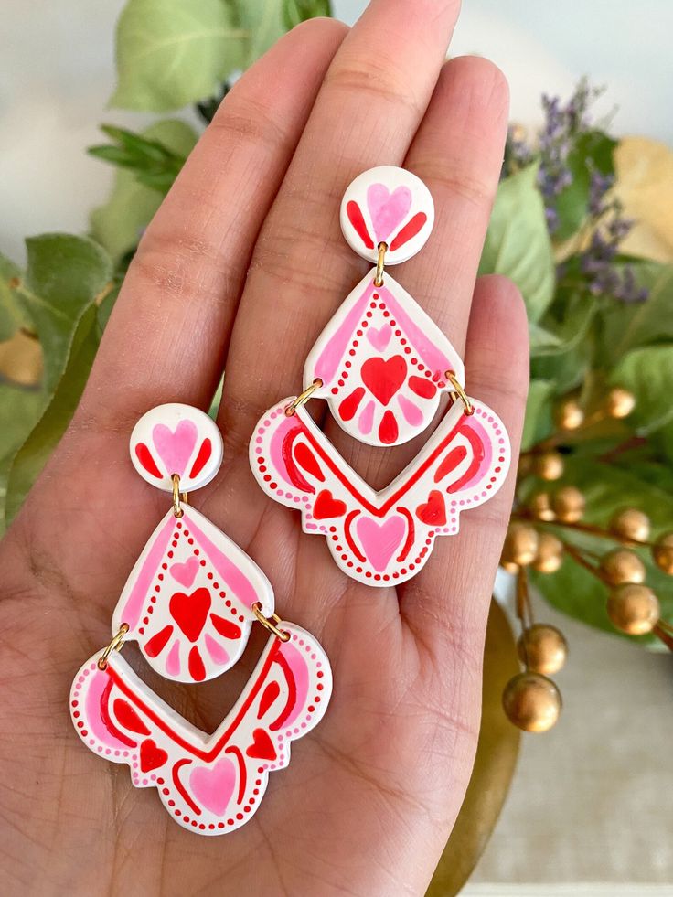 a pair of pink and red earrings on someone's hand with flowers in the background