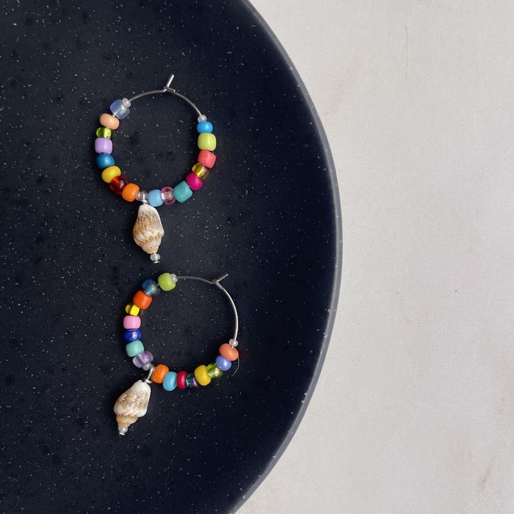 "Vintage sea shell hoops  🍍 SIZING: 25mm (~0.98\") Shell charm is ~0.5\" dangle 🍍 BEADS + MATERIALS: Hypoallergenic, surgical grade steel Stainless steel is tarnish, rust, and moisture resistant Handmade with love 🫶🏼 Vintage y2k shells 🍍 ABOUT these hoops: Made with a variety of colorful seed beads and a vintage y2k shell charm dangling at the center, these silver hoops are sure to be a summer staple 🐳🍌 🍍 DESIGN: Each pair of earrings are made to order. The exact order of the color of the beads may vary slightly, ensuring each pair is one of a kind! 🍍 CUSTOMIZATIONS: If there are any seed bead colors you would like included or don't want, please make a note of that in the personalization section :) 🍍 CARE: * Be gentle when putting in and taking out * Do your best to avoid water a Summer Staples, Beaded Material, Beaded Hoops, Shell Beads, Stainless Steel Earrings, How To Make Notes, Beaded Dangles, Summer Jewelry, Silver Hoops