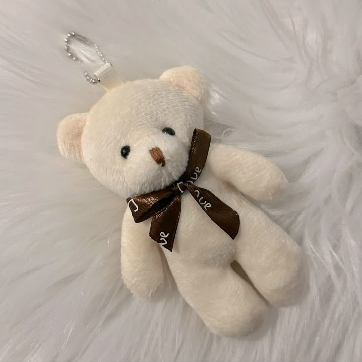 a white teddy bear with a brown ribbon around it's neck sitting on a furry surface