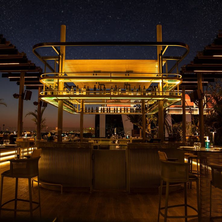 the bar is lit up at night with stars in the sky above it and several stools around it