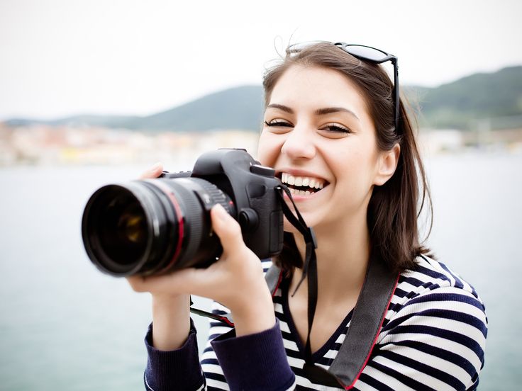 a woman holding a camera up to her face and taking a photo with the water in the background