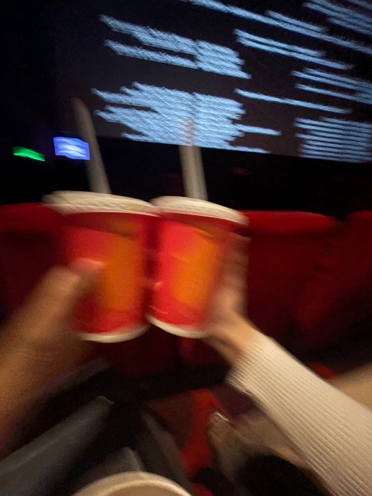 two people holding up red cups in front of a screen