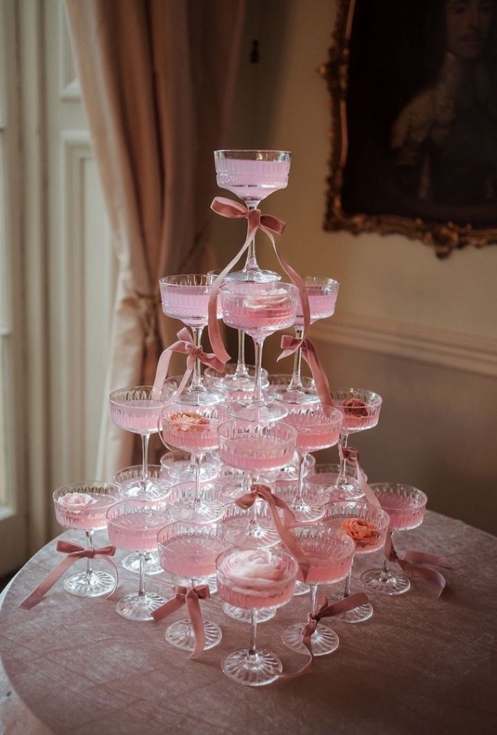 a table topped with lots of glasses filled with pink liquid next to a painting on the wall