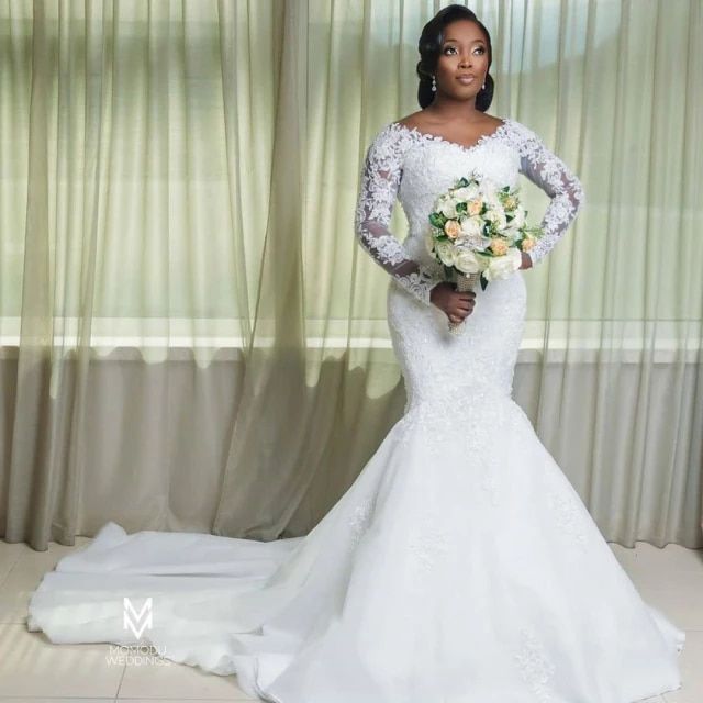 a woman standing in front of a window wearing a wedding dress and holding a bouquet