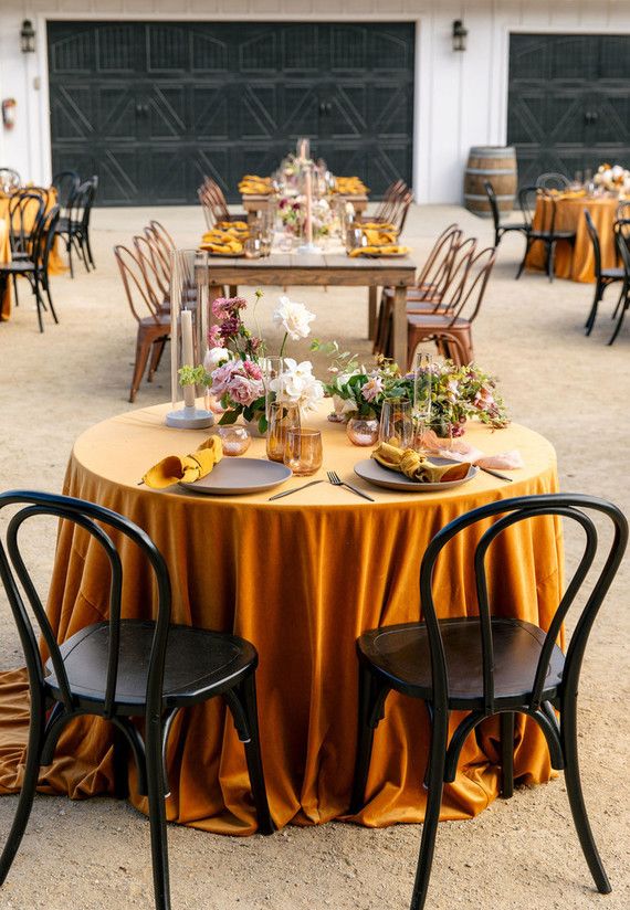 the table is set up with gold cloths and black chairs, along with plates on them