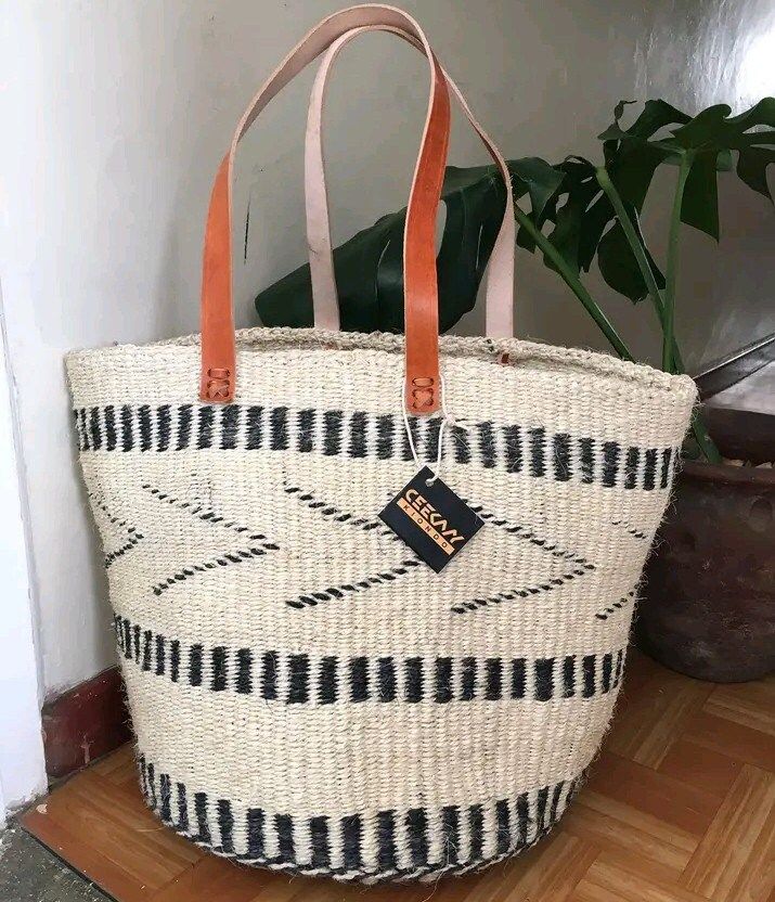 This beautiful handmade Tote bag originated from craftsmen living in Eastern Community in Kenya, the Akamba. Our Tote bags are woven using colored sisal and leather hands.The woven bag is made from products which are entirely eco-friendly and sustainable, leather to provide comfort and padding.  This Tote bag is really stylish, functional and eco-friendly for everyday use, summer travels and beyond. From travel to work or a night out, makes it easier to fill your closet with ethical, high quality staples for every occasion. It's dimensions are approximately; 14" W  x 14" H(excluding the handle). As African I stores, we are very pleased and proud of the fact that  each bag we bring in to your life provides support for Kenyan craftsmen and their families and contributes to the continuation o Woven Beach Bag, Woven Beach Bags, African Bag, Handmade Tote Bag, Nairobi Kenya, Sustainable Leather, Office Bag, Handmade Tote, Woven Tote Bag