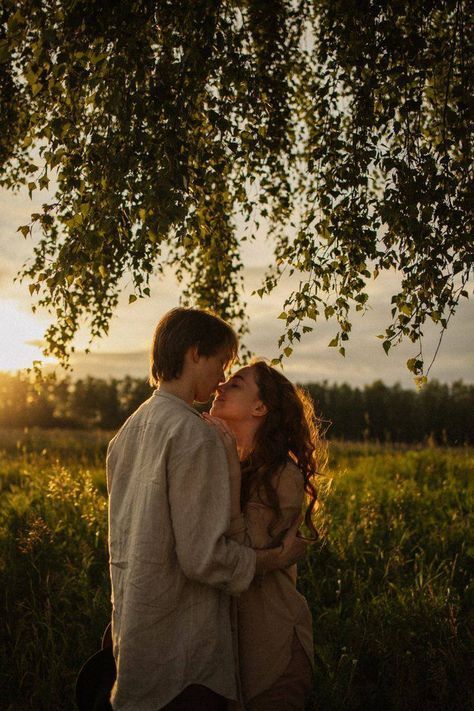 a man and woman kissing under a tree in a field at sunset with the sun behind them