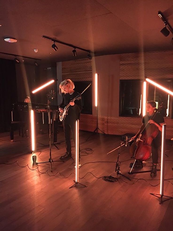 three people playing instruments in a room with lights on the wall and wood flooring