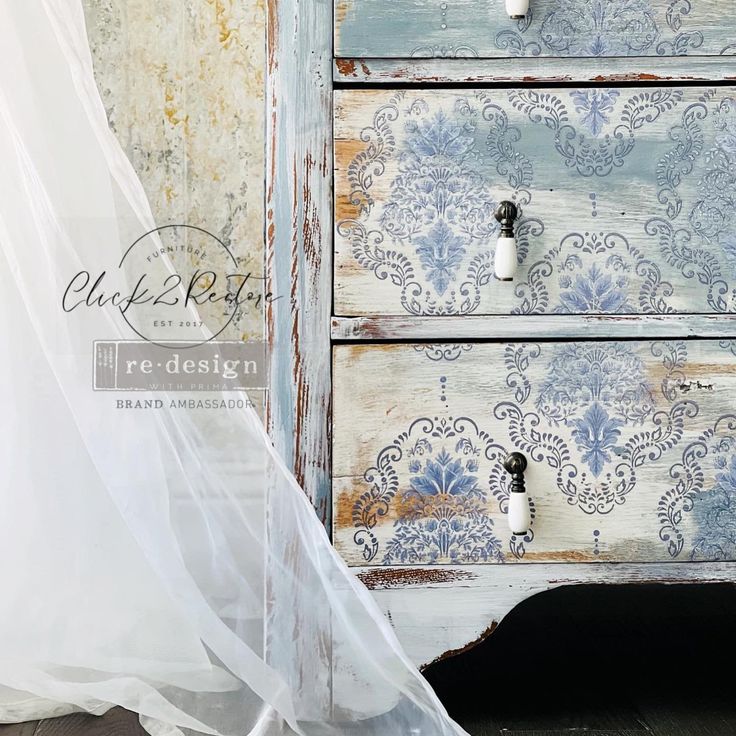 an old dresser has been painted with blue and white floral wallpaper, along with a sheer curtain