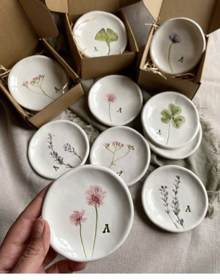 a hand holding a set of six plates with flowers painted on them in front of boxes