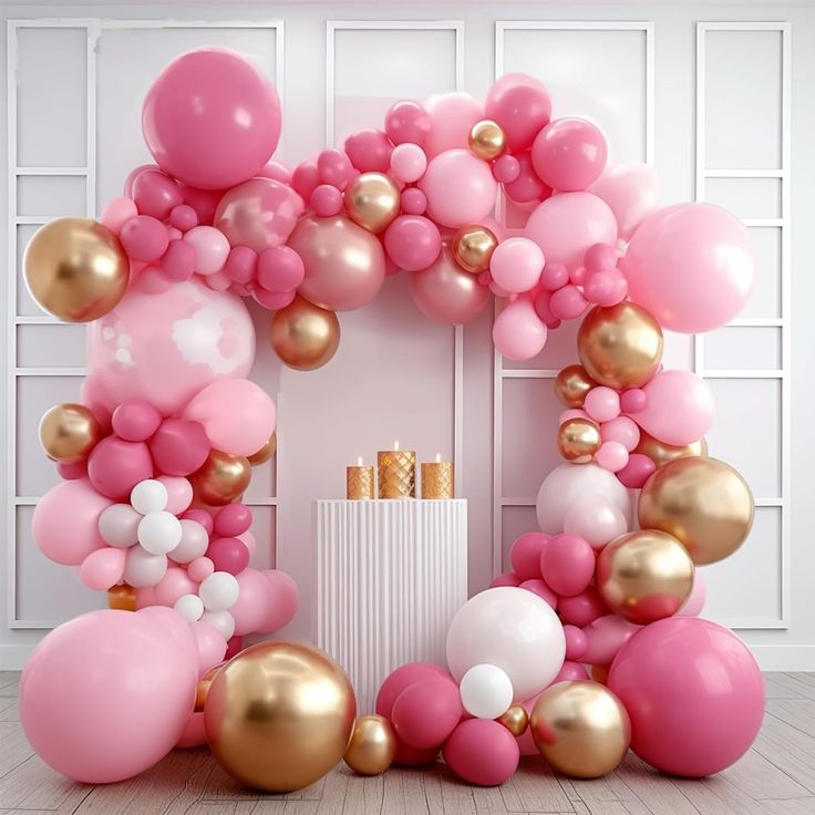 a pink and gold balloon arch in front of a white wall