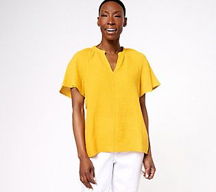 a woman standing in front of a white background wearing bright yellow shirt and white pants